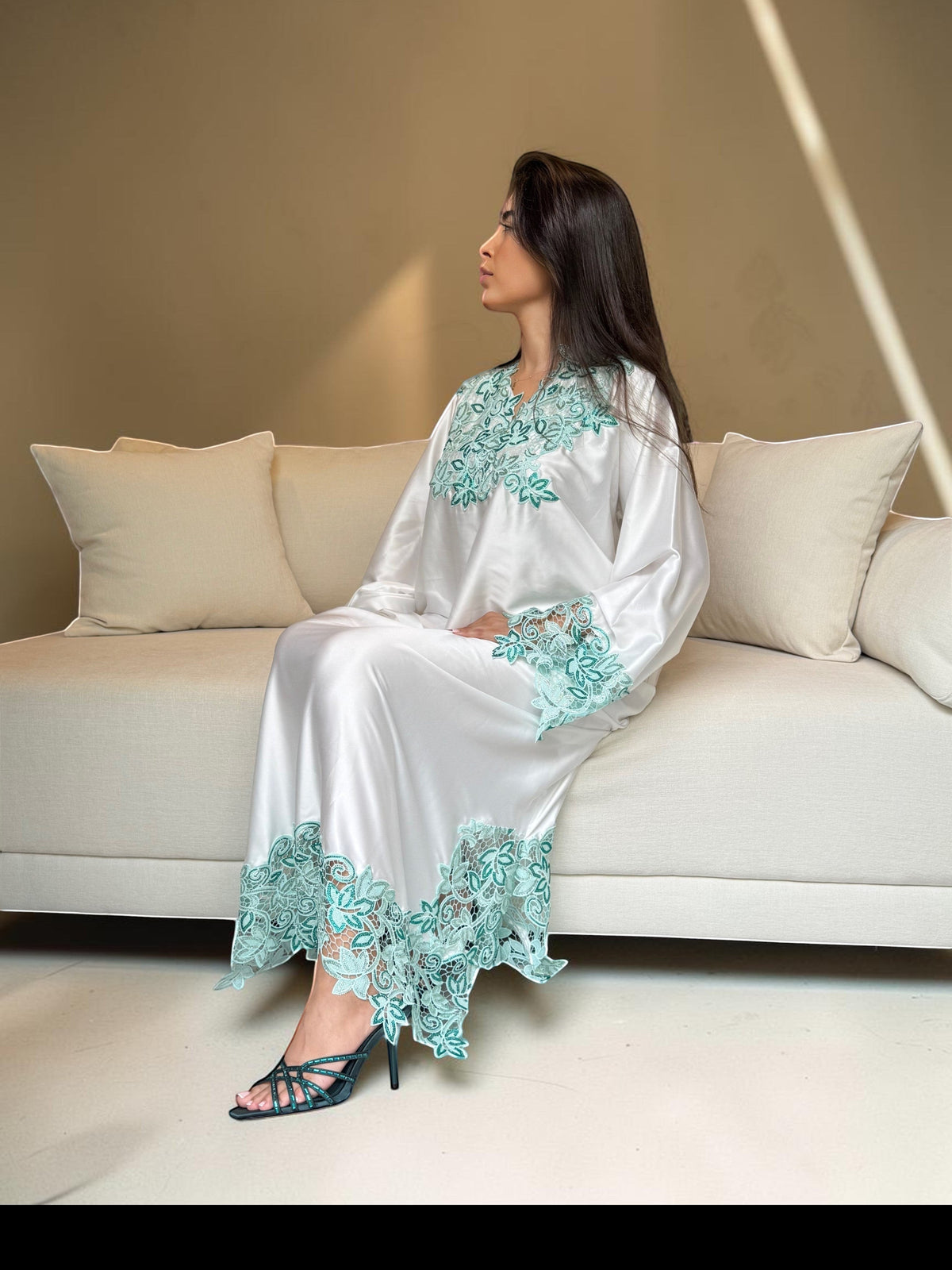 ABAYAS white Nida lace dress with emerald and turquoise floral embroidery on neckline, sleeves, and hem. Elegant, long-sleeved, floor-length.
