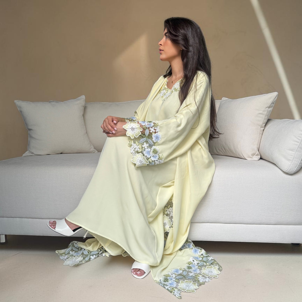 ABAYAS yellow Nida abaya with floral lace on sleeves and hem, open front, matching inner dress. Model seated on couch.